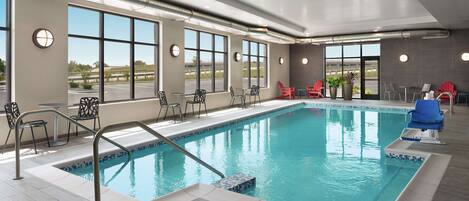 Une piscine intérieure offrant une vue dégagée grâce à de grandes fenêtres, entourée d’espaces de détente et dotée d’un aménagement intérieur moderne.