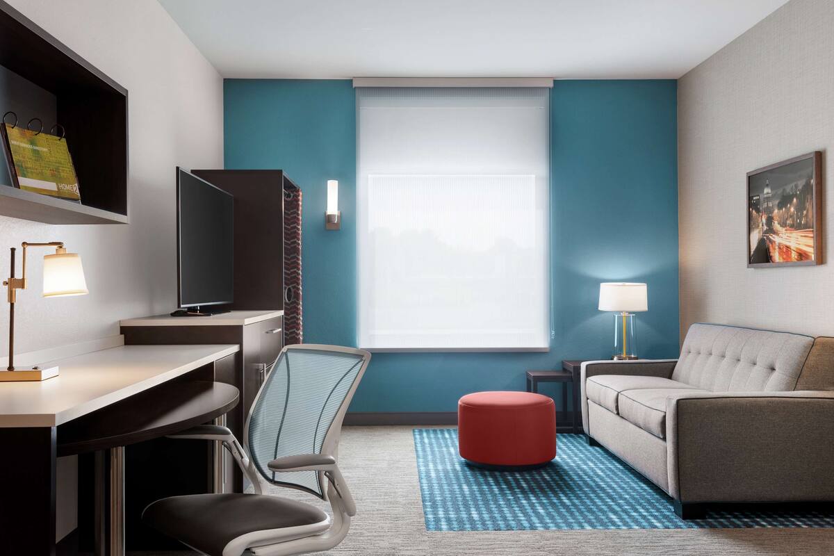 Een moderne hotelkamer met een bureau, stoel, bank en poef.