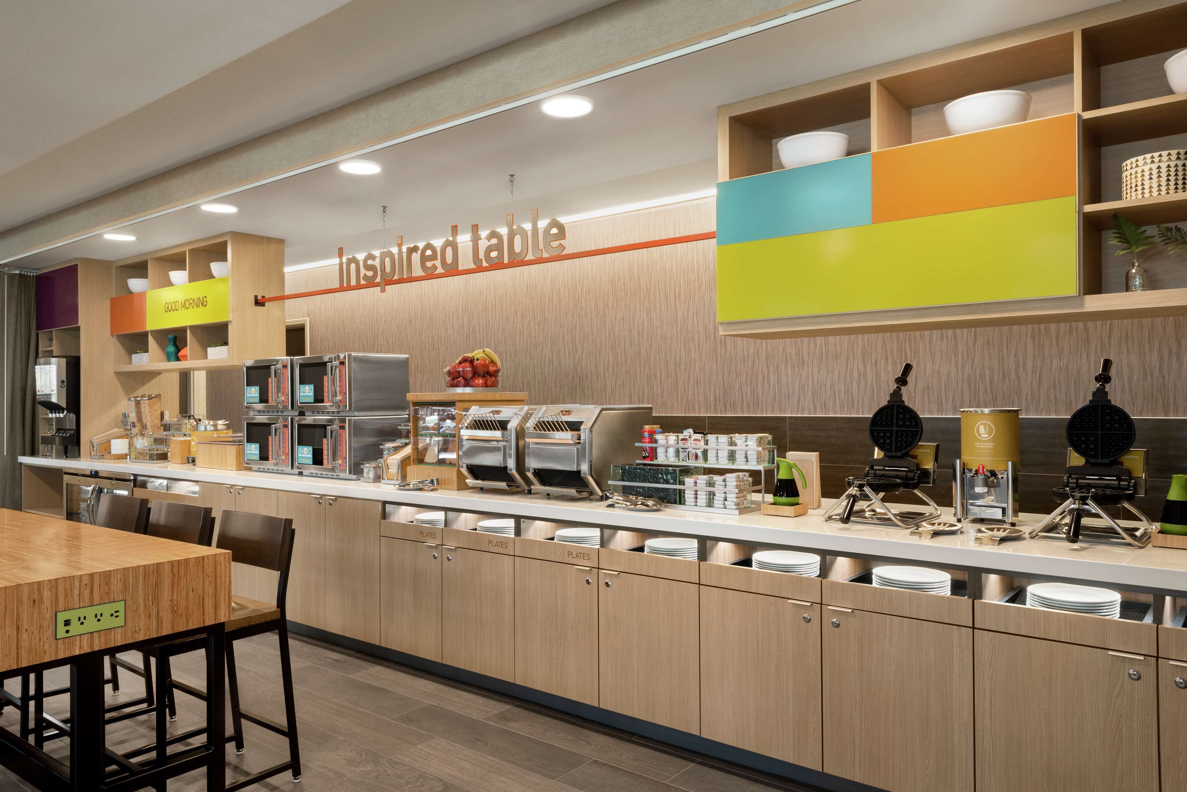 Una barra de desayuno con un cartel que dice "inspired table", una máquina de café, una máquina para hacer gofres y diversas opciones de desayuno.