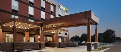 A hotel with a covered entrance, a sign reading "HOME 2 SUITES," and a parking lot.
