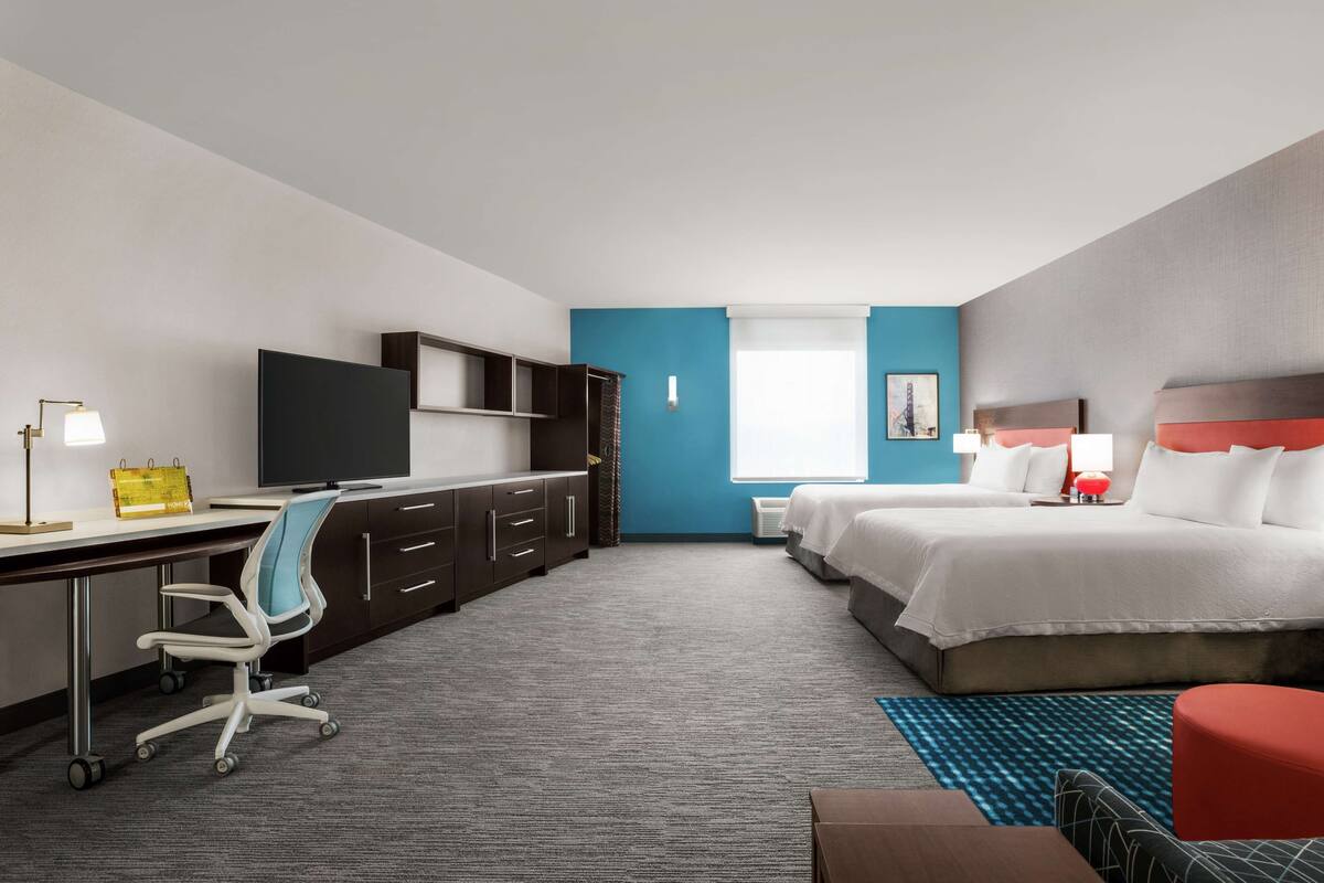 Een hotelkamer met een bureau, twee bedden, een televisie en een raam met uitzicht.