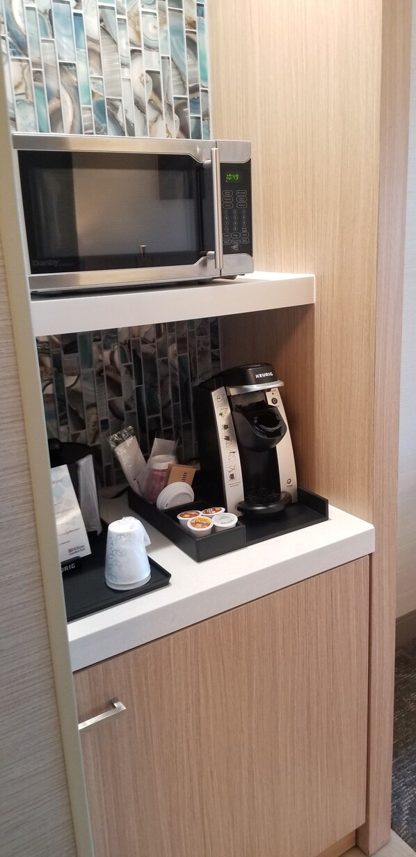 A kitchenette with a microwave, Keurig coffee maker, and a coffee cup.