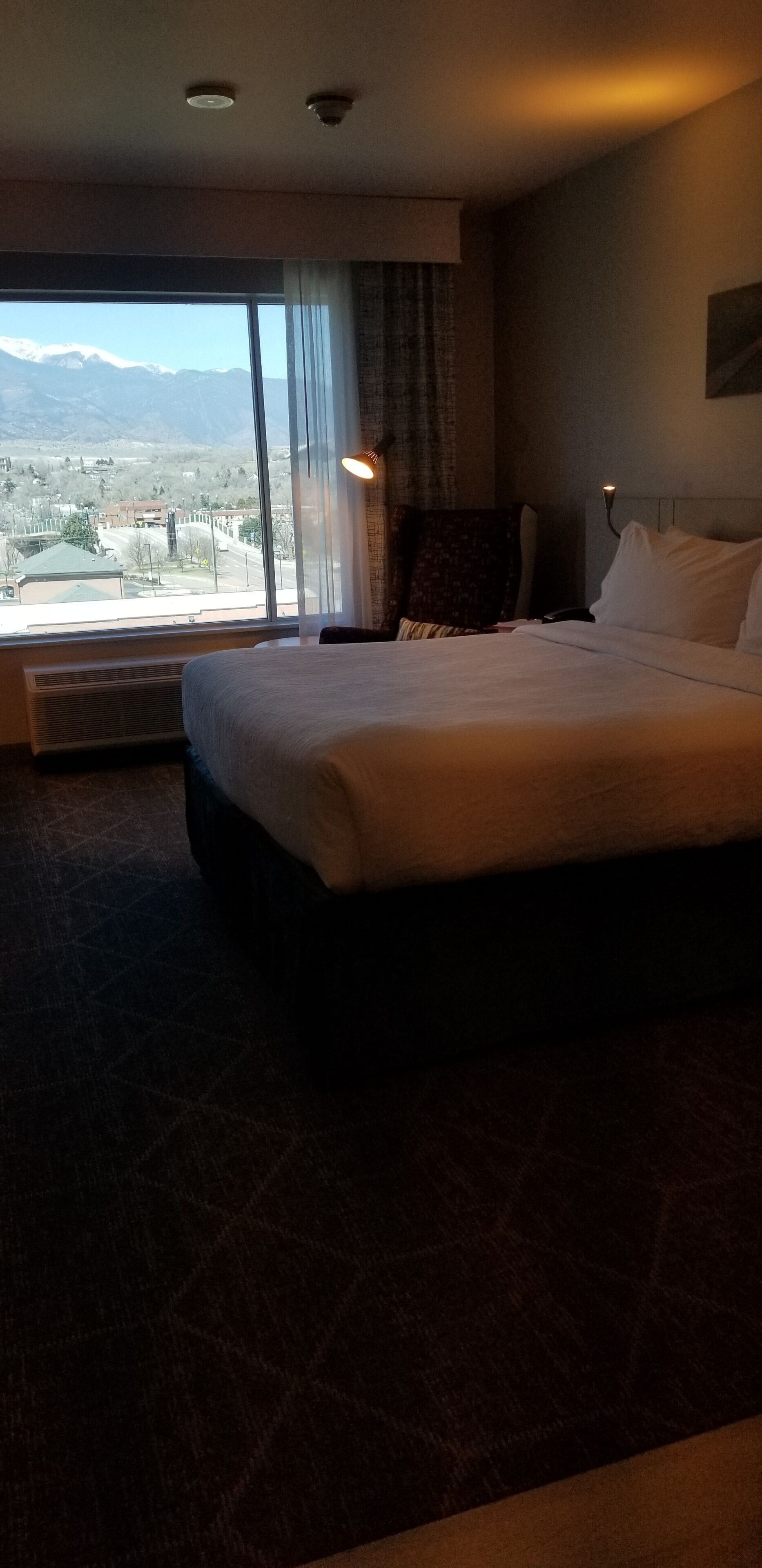Une chambre d’hôtel avec un grand lit, une vue sur les montagnes par la fenêtre et un plafond doté d’un éclairage encastré.