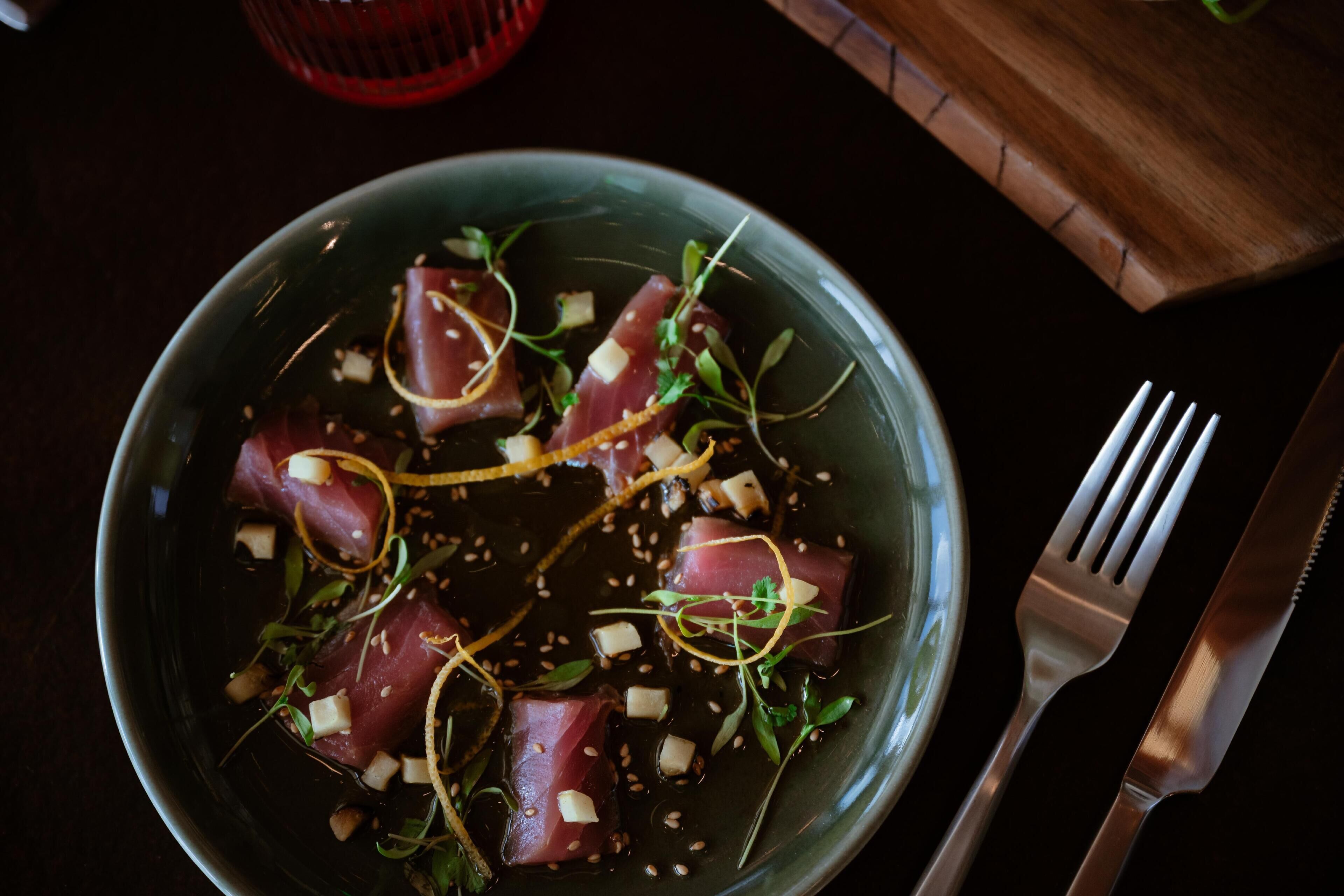 A bowl of sashimi with sesame seeds and green garnish.