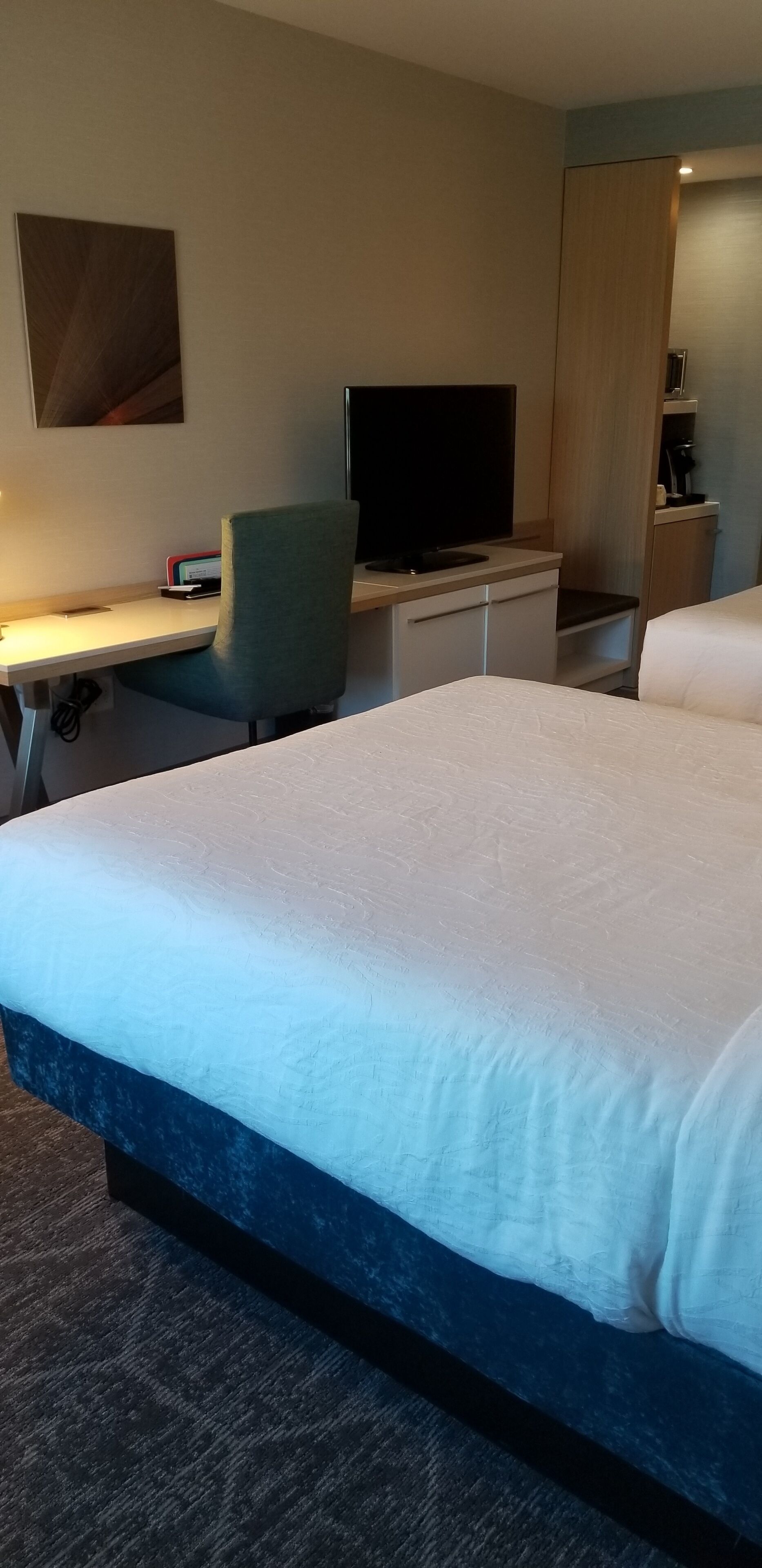 A hotel room with a large bed, a desk with a chair, a television, and a wardrobe.