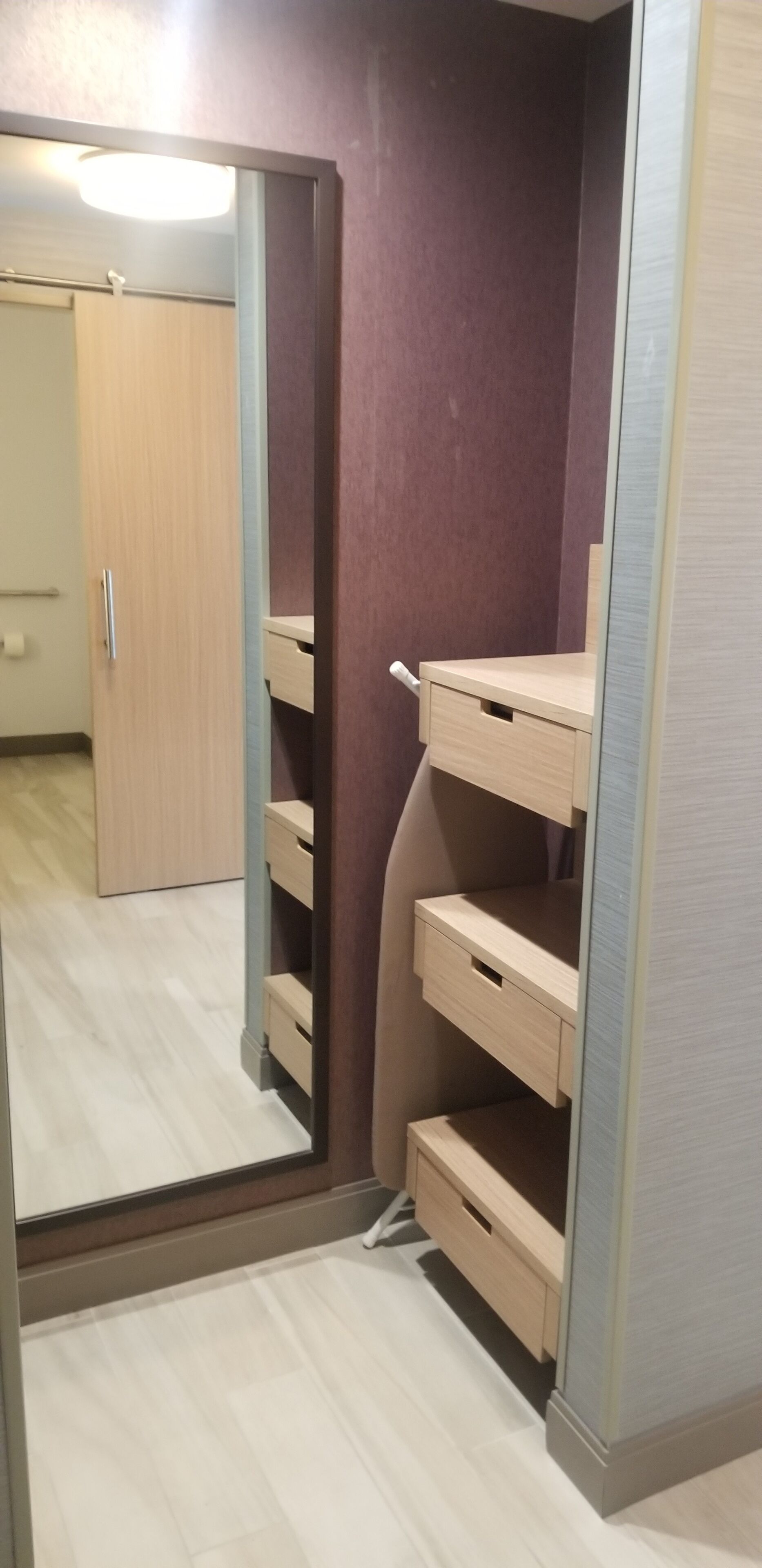 A room with a wooden wardrobe, a mirror, and a light-colored floor.