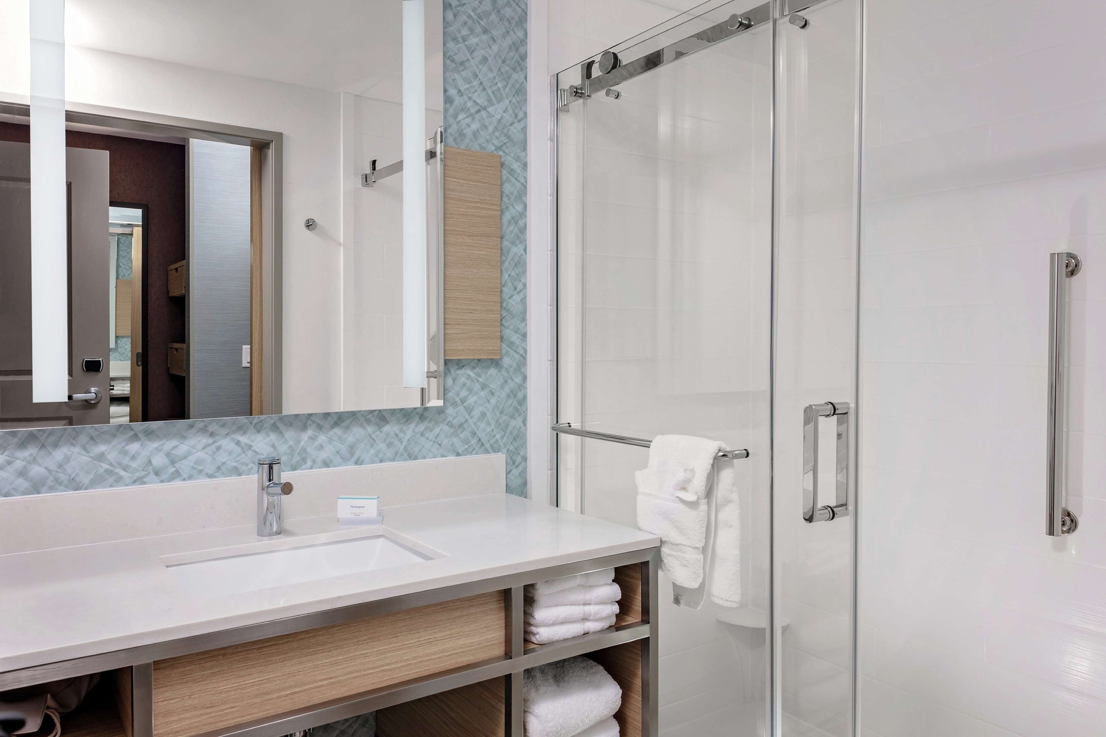 A modern bathroom with a large mirror, a sink, a glass shower enclosure, and a towel rack.