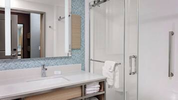 A modern bathroom with a large mirror, a sink, a glass shower enclosure, and a towel rack.