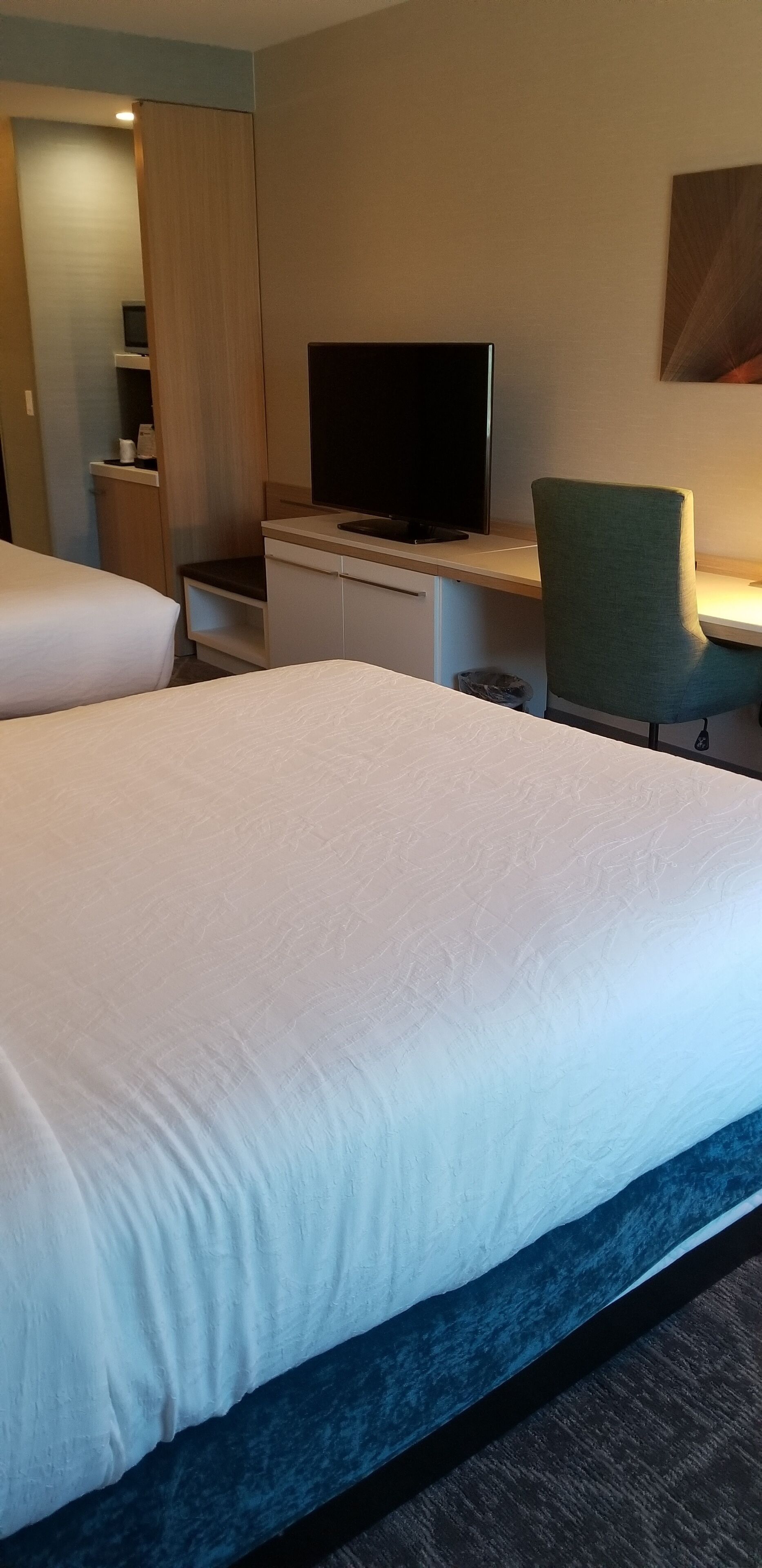 A hotel room with a large bed, a desk with a flat-screen TV, a green chair, and a wardrobe.