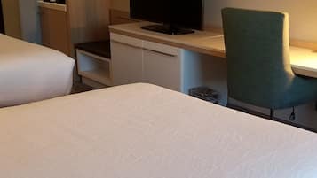 A hotel room with a large bed, a desk with a flat-screen TV, a green chair, and a wardrobe.