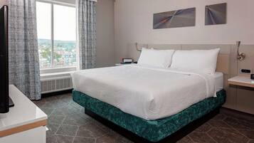 A hotel room with a large bed, a desk, a flat-screen TV, a window with curtains, and two wall-mounted artworks.