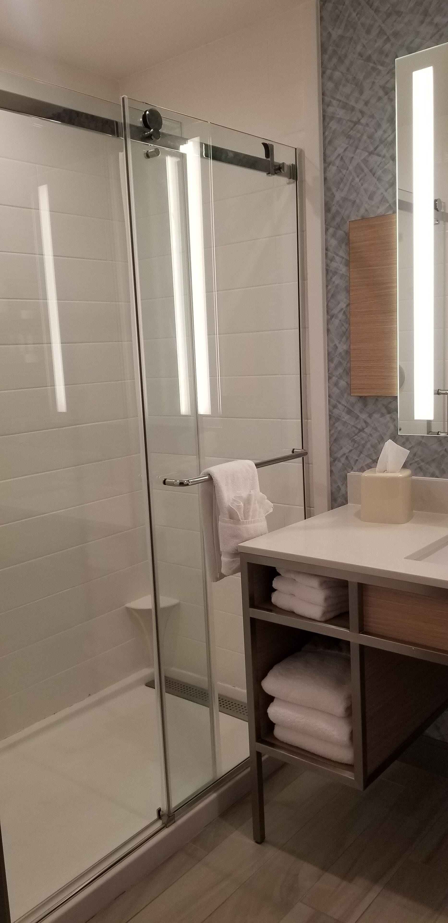 Ein modernes Badezimmer mit Duschkabine aus Glas, einem Holzbadezimmer-Möbel und einem Handtuchhalter.