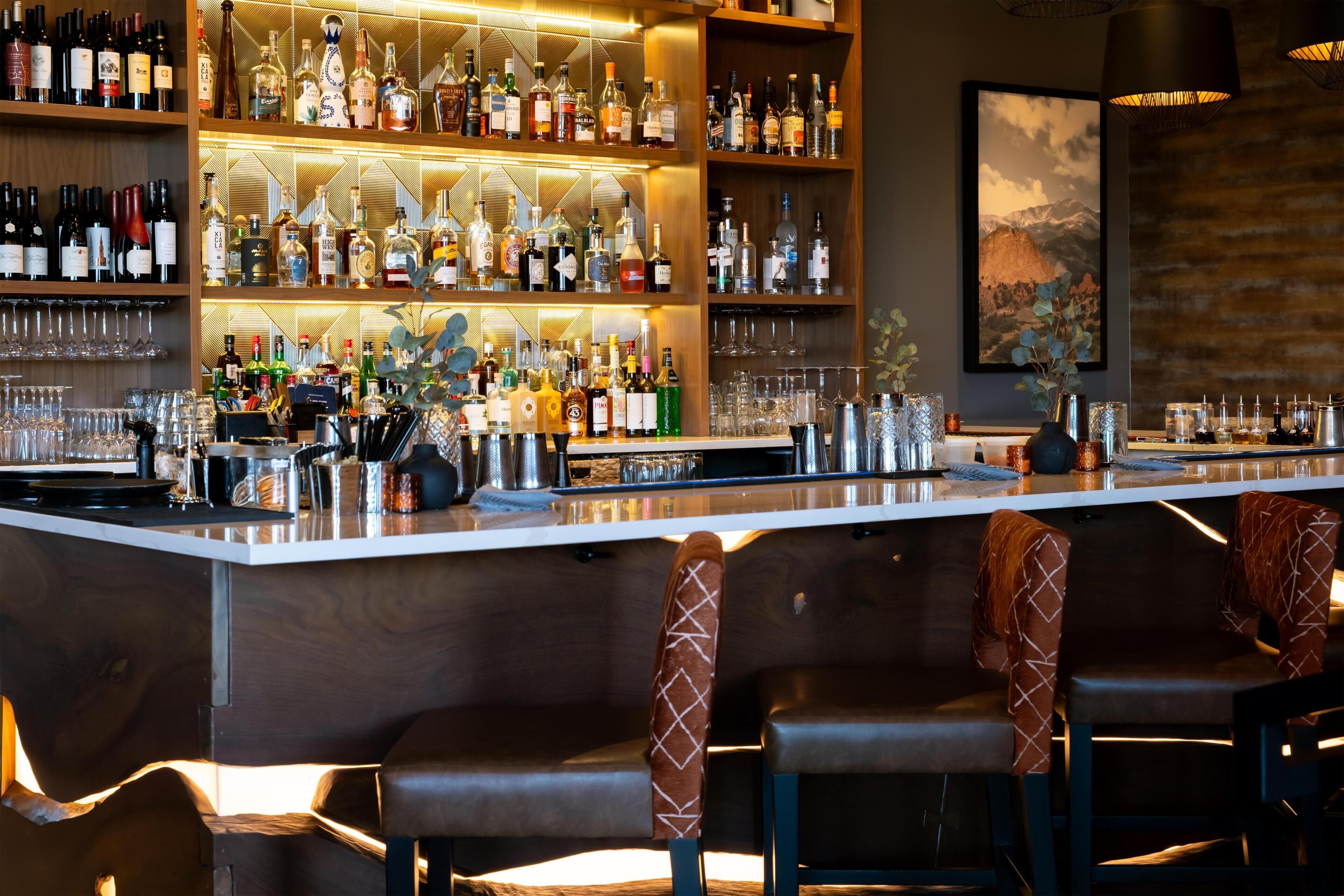 Un espace bar avec des étagères remplies de bouteilles d’alcool, de verres et un comptoir.