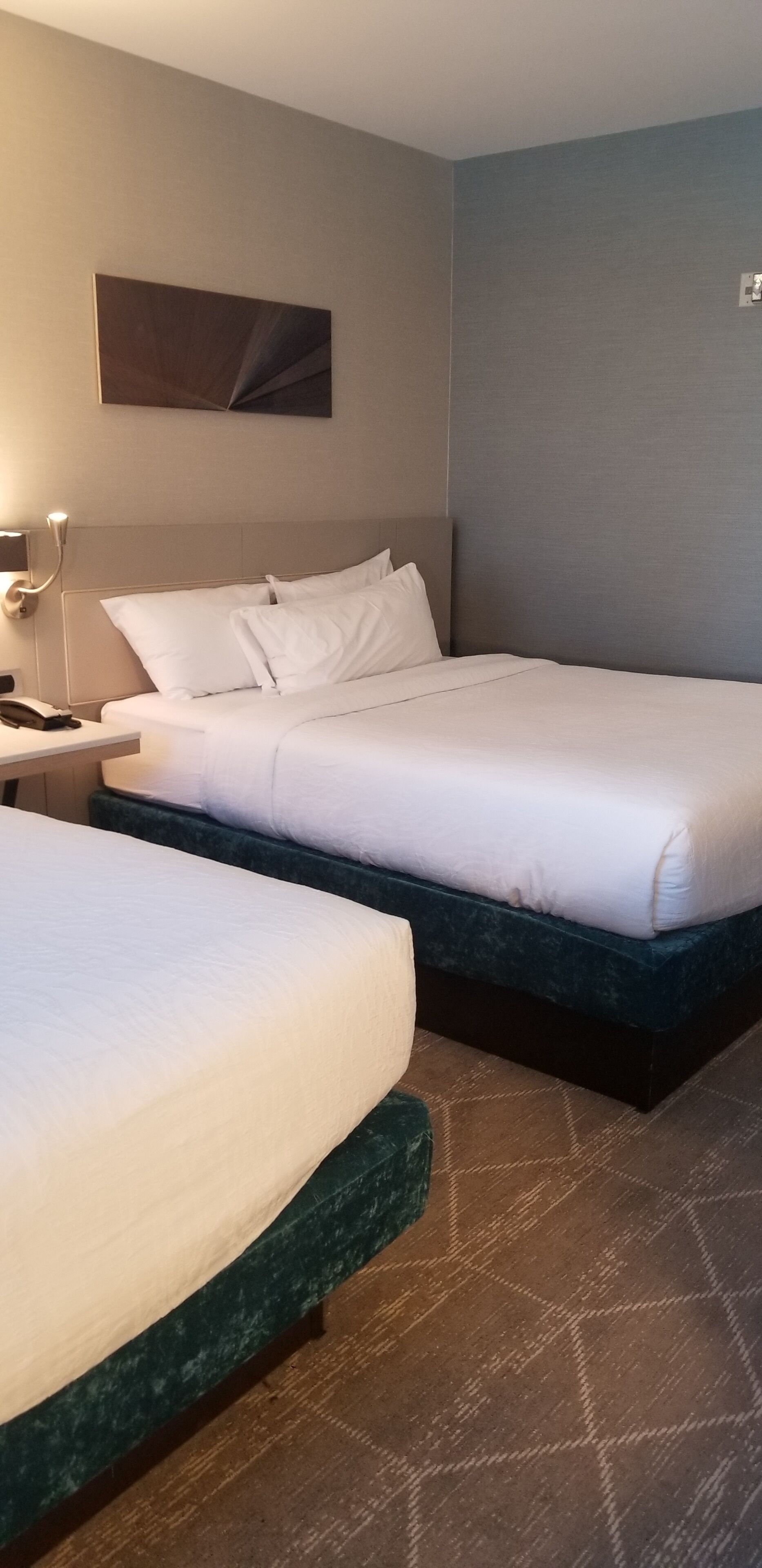 A hotel room with two beds, a nightstand with a lamp, and a painting on the wall.