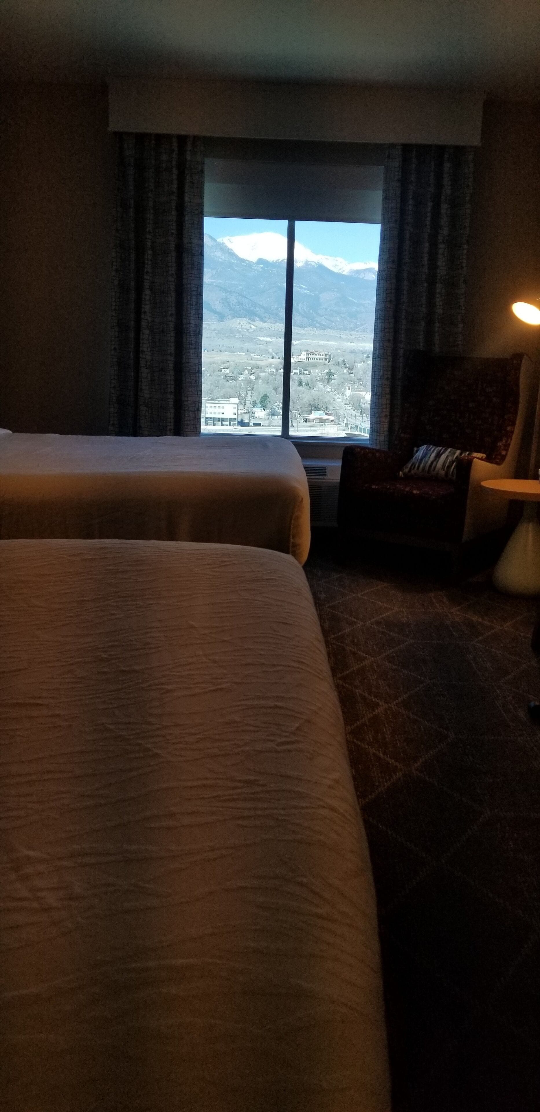 A hotel room with two beds, a view of mountains, and a chair with a pillow.