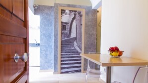 Une cuisine moderne avec une table et des chaises en bois, un panier de fruits et une vue sur un escalier en pierre menant à un balcon.