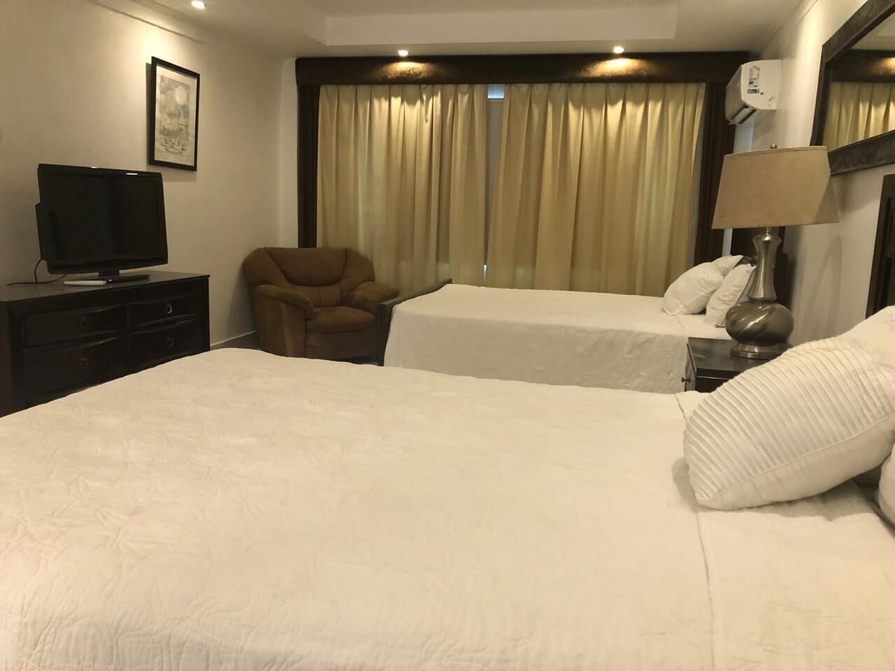 Une chambre d’hôtel avec deux lits, un téléviseur posé sur une commode, une chaise et une lampe.