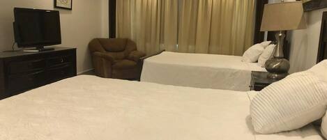 Une chambre d’hôtel avec deux lits, un téléviseur posé sur une commode, une chaise et une lampe.