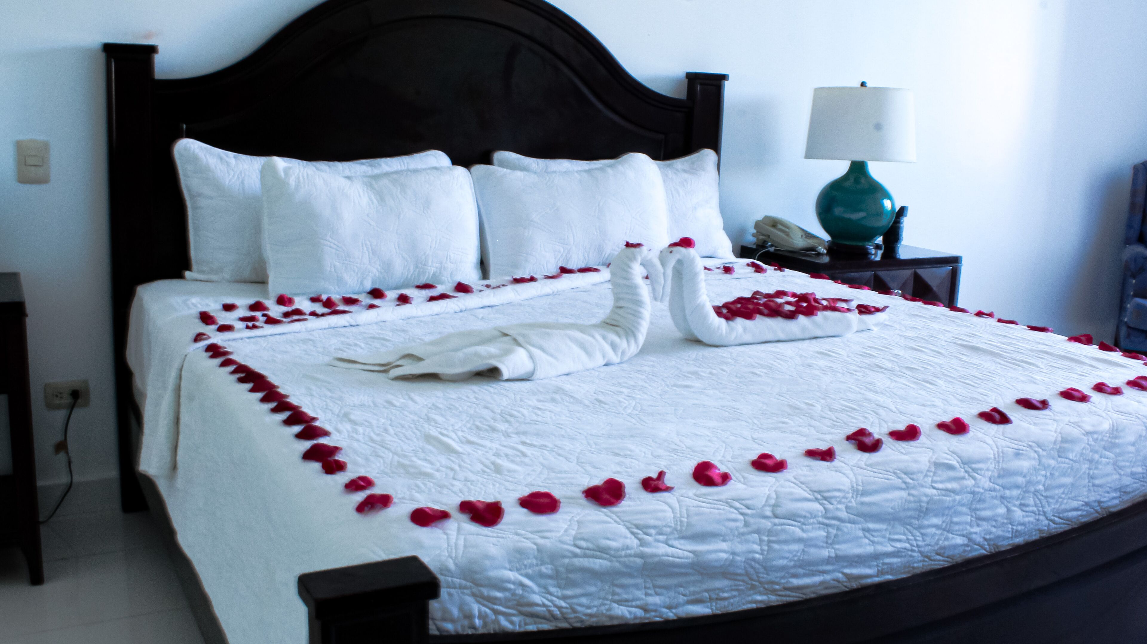 Una cama impecablemente hecha con ropa blanca y pétalos de rosa dispuestos en forma de corazón.