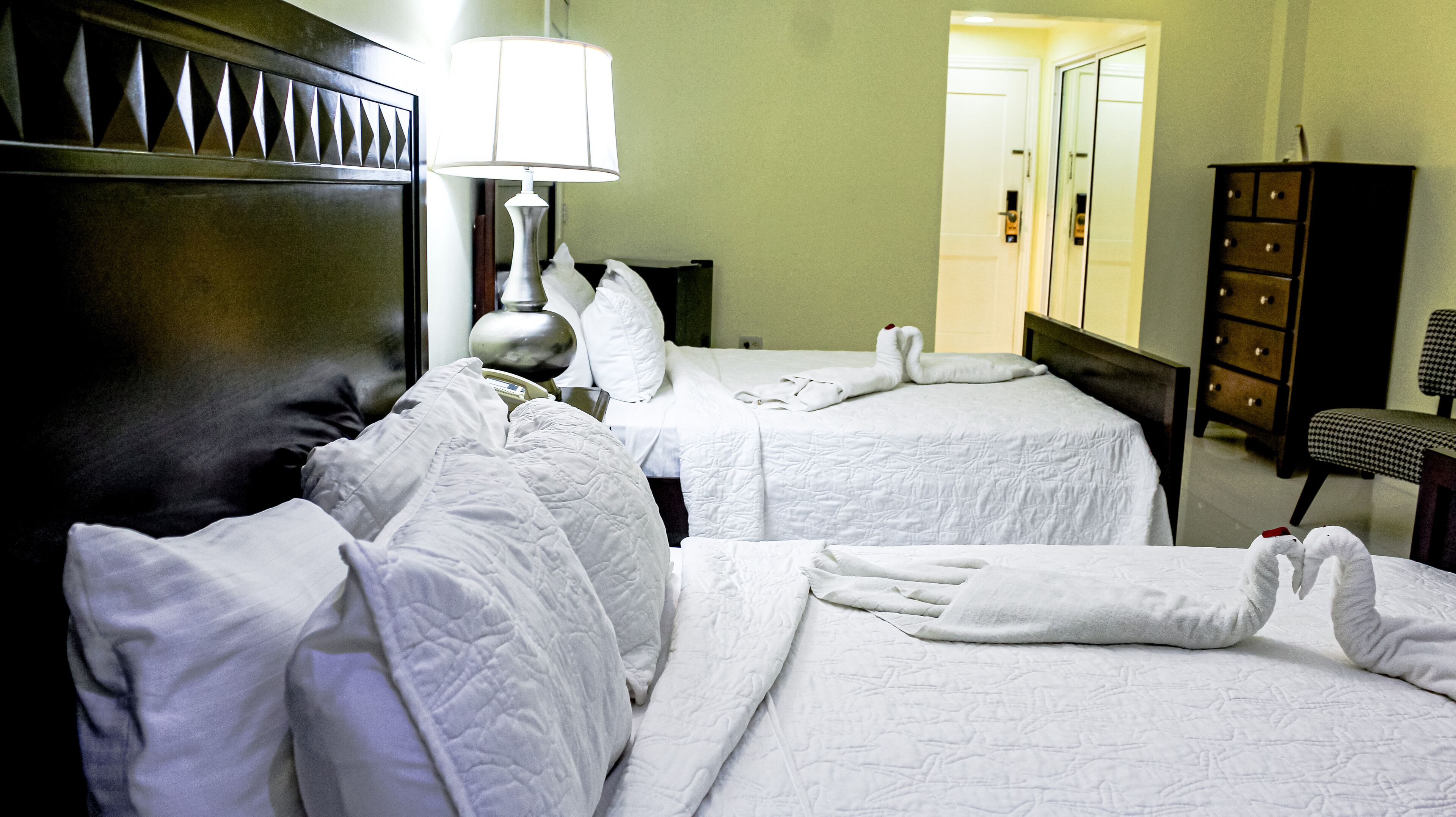A hotel room with two beds, a lamp, a dresser, and a chair.
