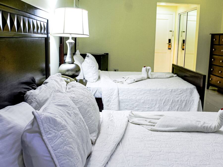 A hotel room with two beds, a lamp, a dresser, and a chair.