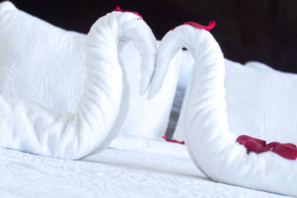 Ein Bett mit weißer Bettwäsche und einer herzförmigen Handtuchgestaltung.