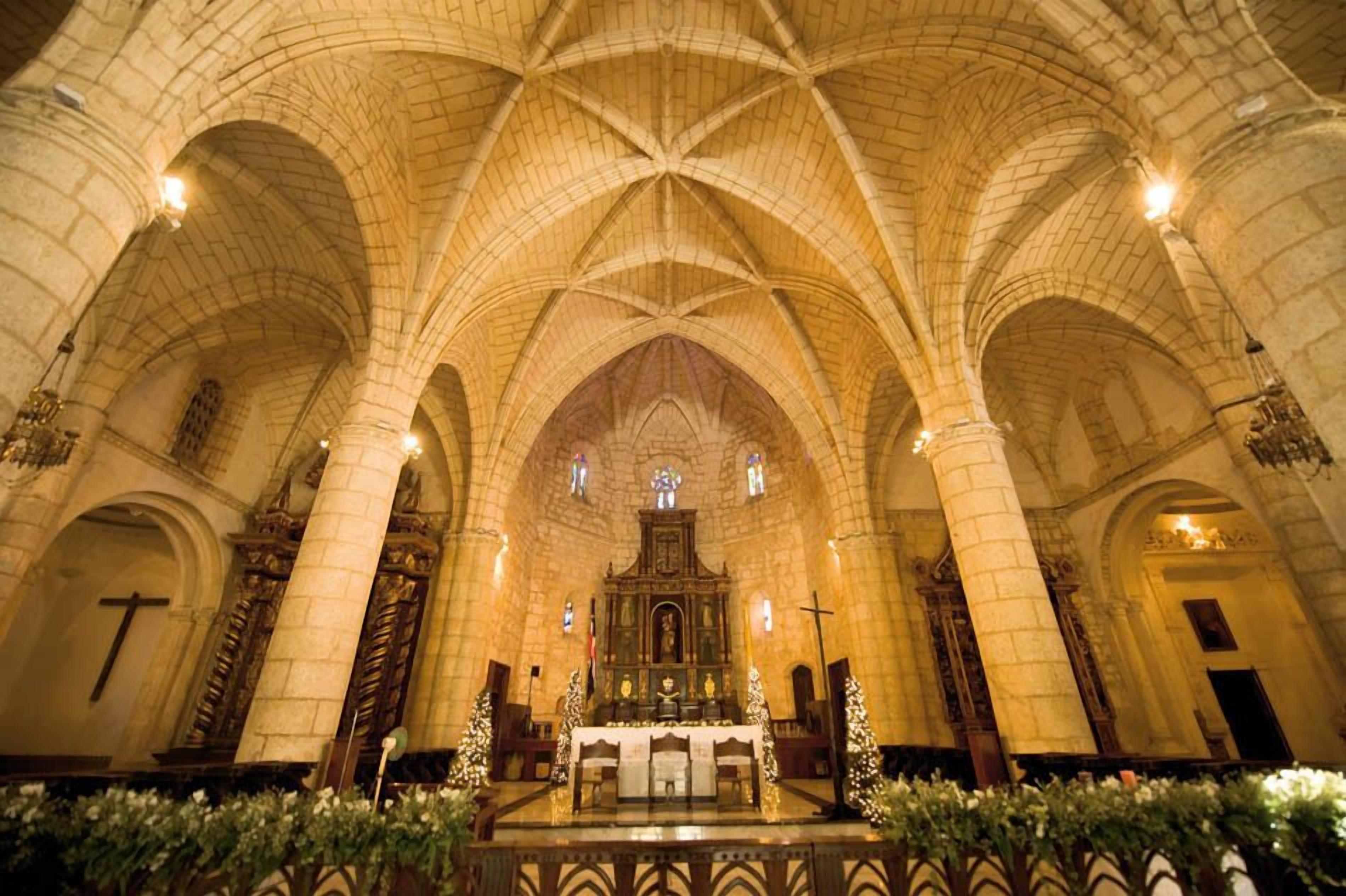 Interior de una catedral con altos techos abovedados, un altar central y hileras de bancas.
