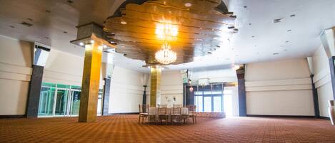 A spacious hall with a patterned carpet, a chandelier, and a table set for dining.
