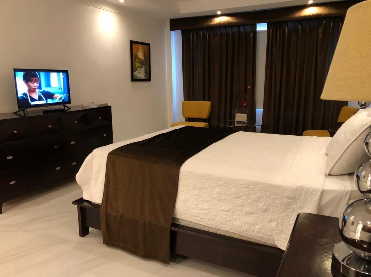 A hotel room with a bed, a TV, a dresser, and a lamp.