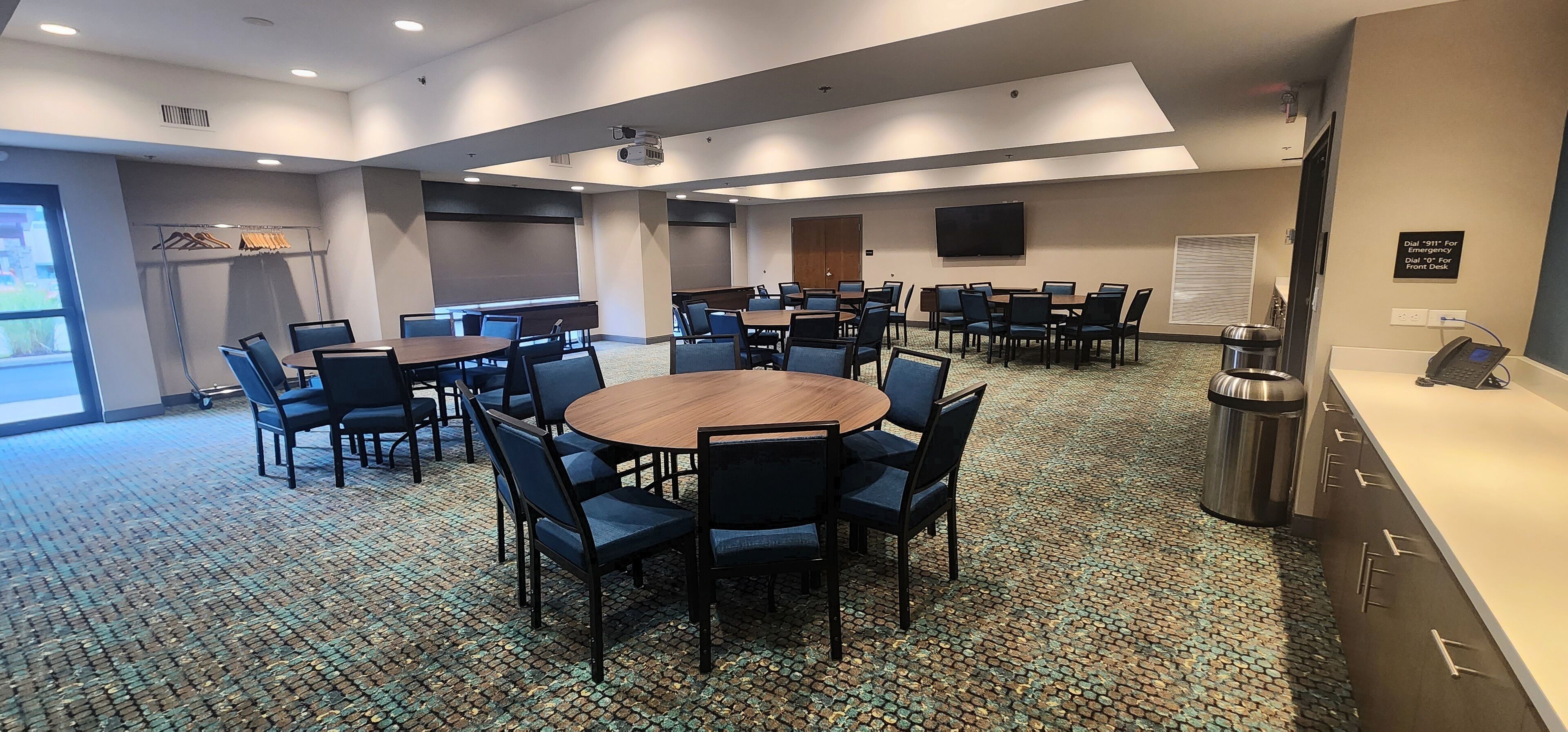 A conference room with multiple tables and chairs, a projector, a TV, and a trash can.