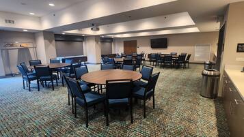 A conference room with multiple tables and chairs, a projector, a TV, and a trash can.