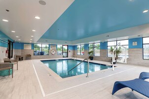 Una piscina interior con agua cristalina, rodeada de sillas de descanso y un letrero de salvavidas.
