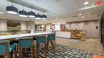 A modern hotel lobby with a reception desk, a 'Welcome to Ohio's Wine Country' sign, a seating area with a sofa and chairs, and a patterned rug on the floor.