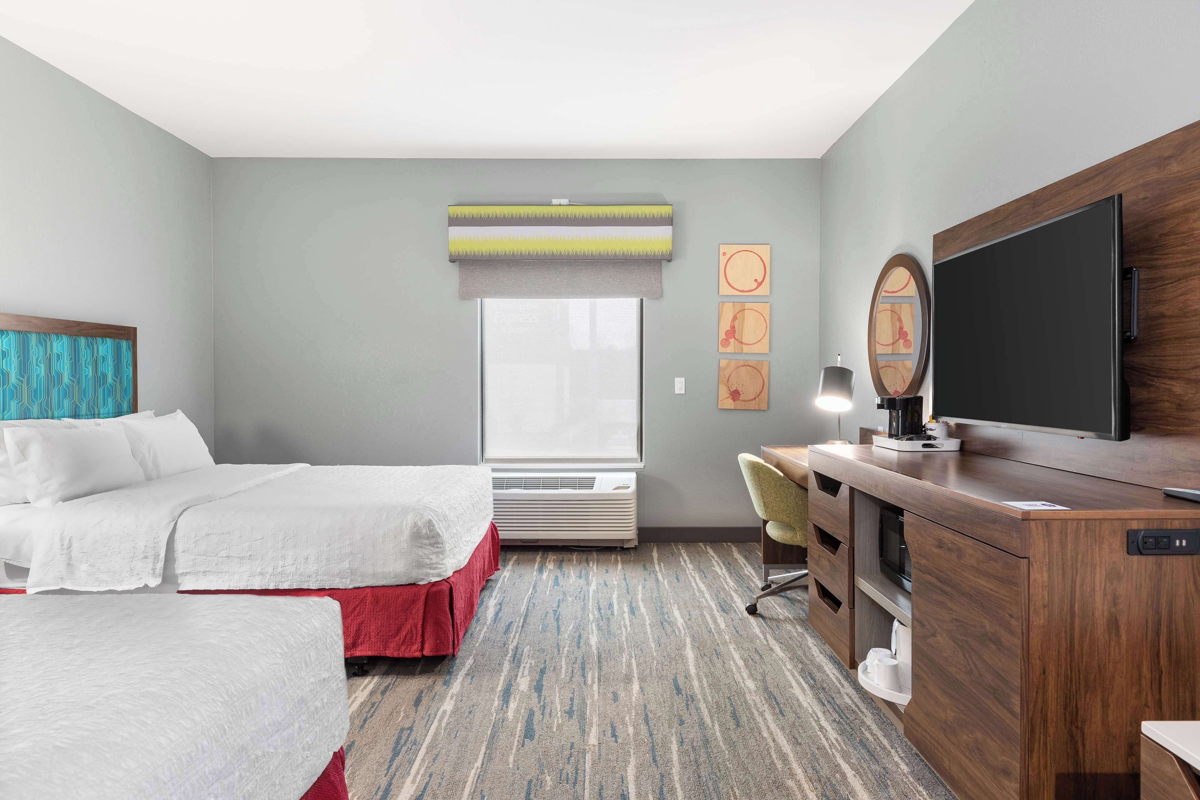 A hotel room with two beds, a desk, a television, and a window with blinds.