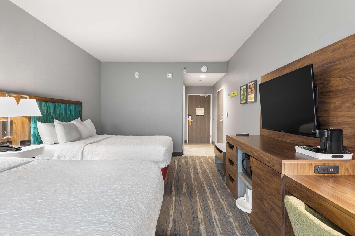 A hotel room with two beds, a desk with a television, and a coffee maker.