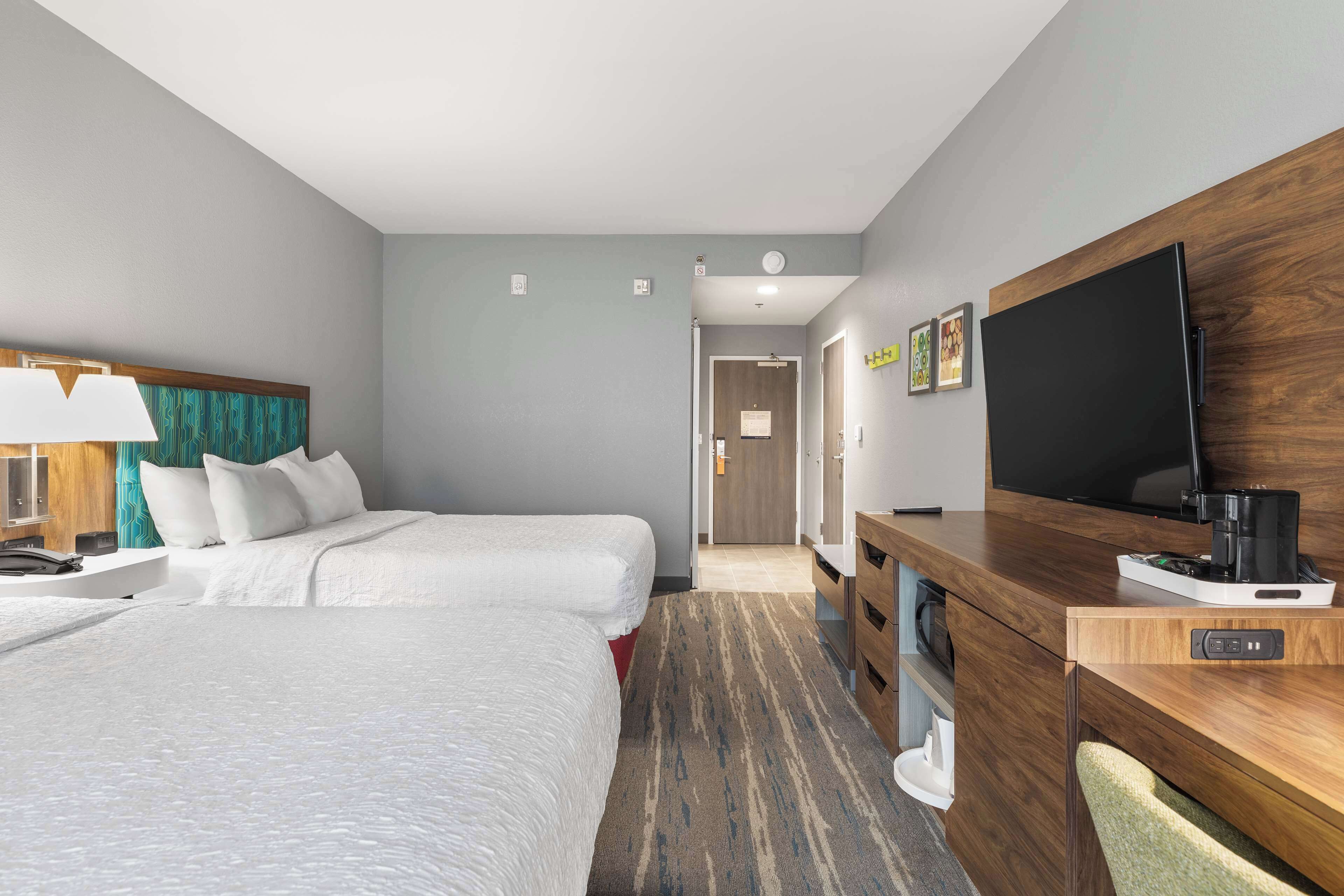 A hotel room with two beds, a desk with a TV, and a coffee maker.