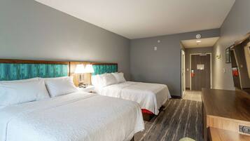 A hotel room with two beds, a desk, a chair, and a bathroom visible through an open door.