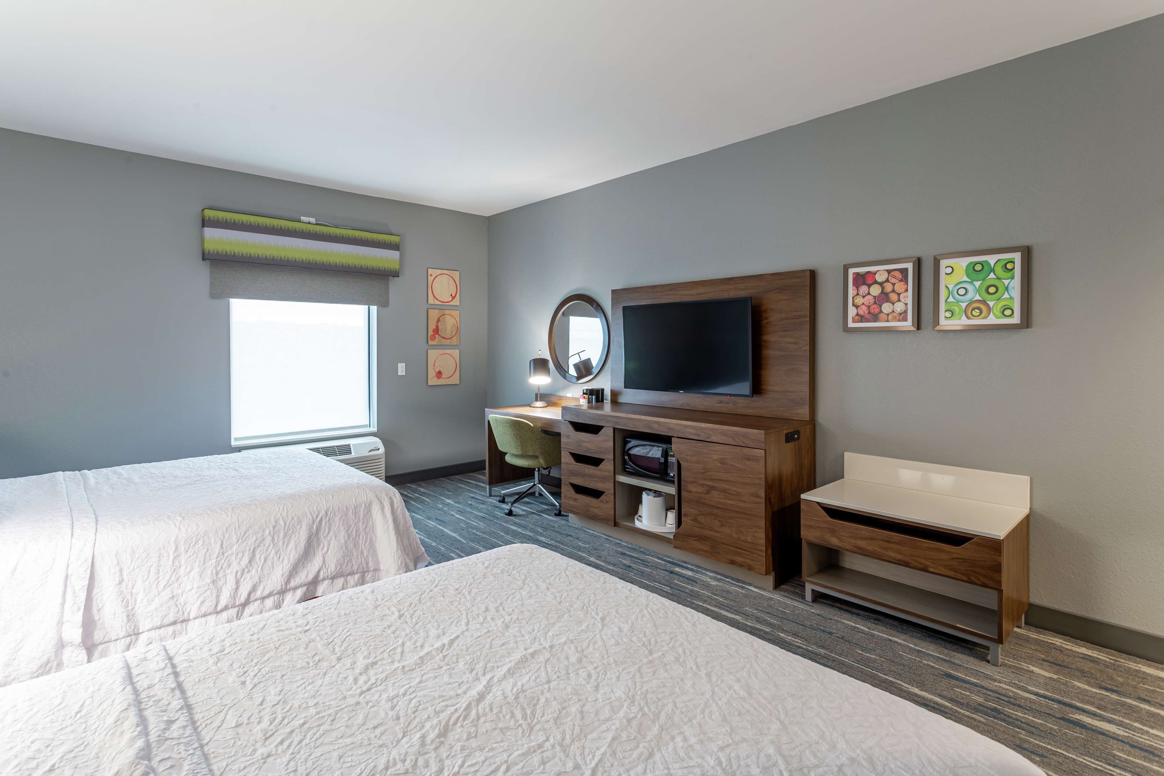 A hotel room with two beds, a desk with a chair, a TV, and artwork on the walls.