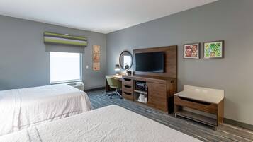 A hotel room with two beds, a desk with a chair, a TV, and artwork on the walls.
