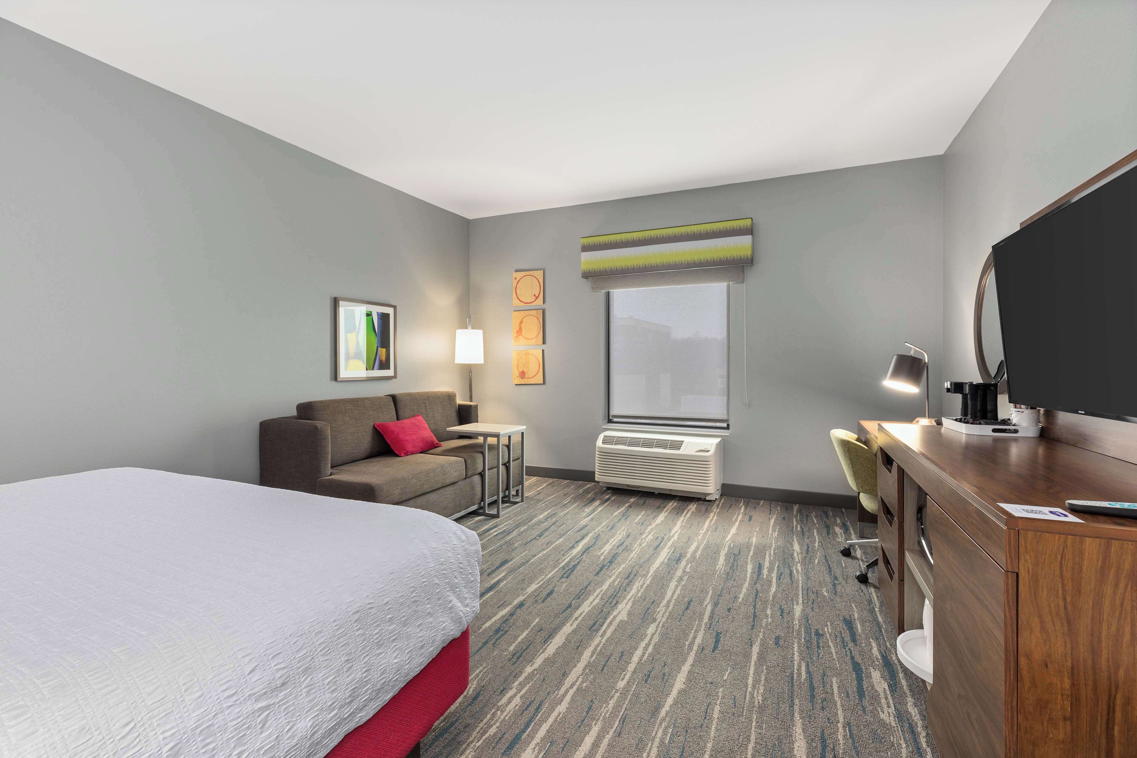 Une chambre d’hôtel avec un lit, un bureau, une chaise, une télévision et une fenêtre.