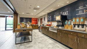 A modern kitchen area with a counter, coffee machines, and a chalkboard wall with menu items. - Hampton Inn Madison (Madison)