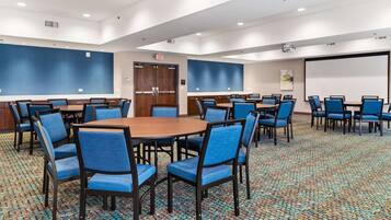 A conference room with round tables and blue chairs, a projector screen, and a large door.
