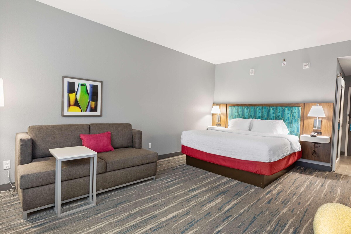 A hotel room with a bed, a sofa, a small table, and a nightstand with lamps.