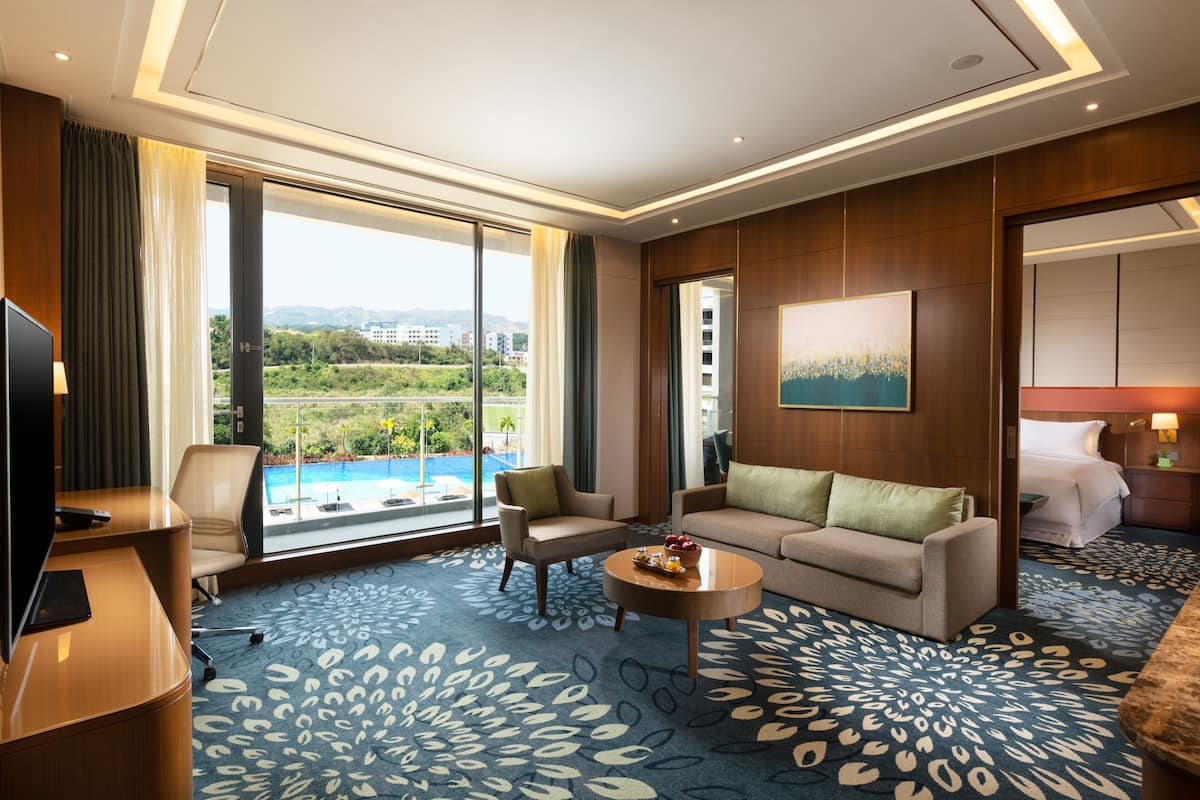 A hotel room with a large window, a sofa, a coffee table, and a TV.