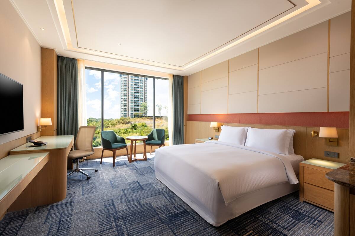 A hotel room with a large bed, a desk, a chair, a small table, and a TV.