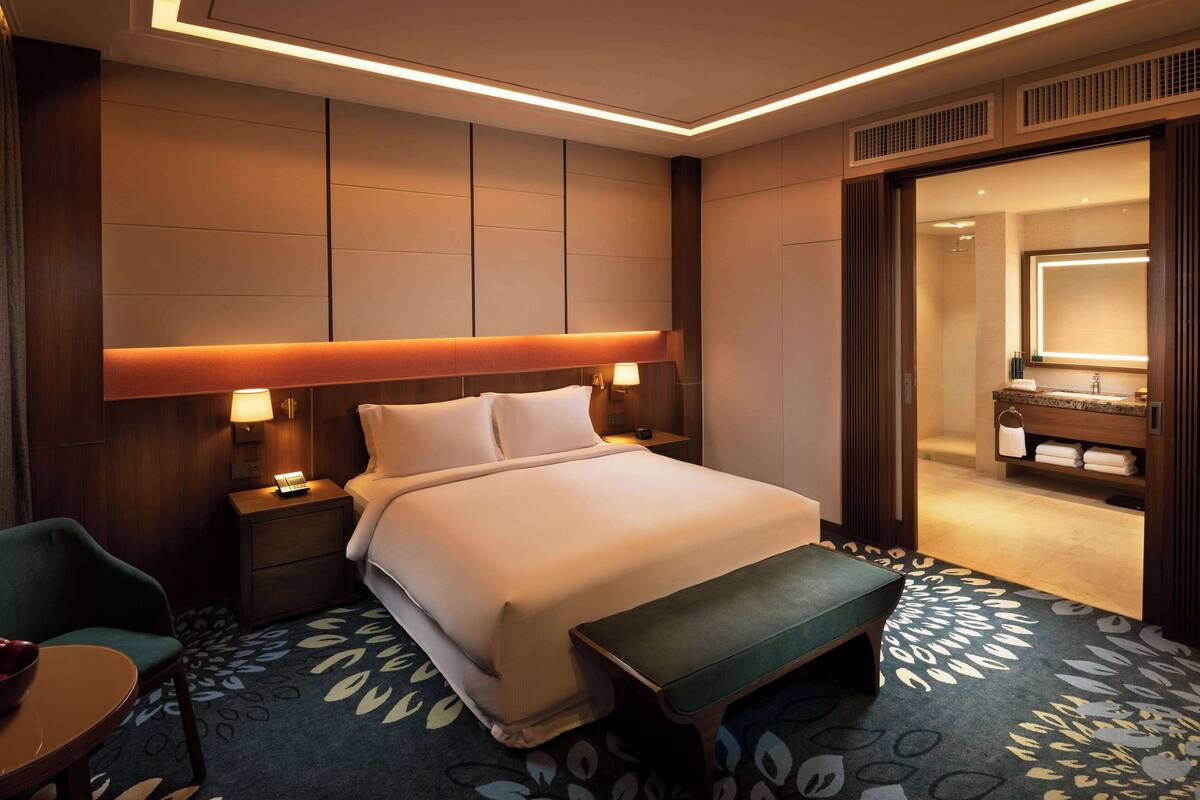 A hotel room with a large bed, bedside lamps, a small table, and a patterned carpet.