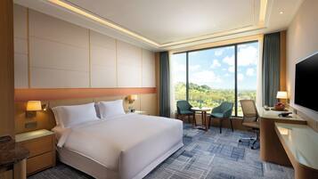 Habitación de hotel con una cama grande, un escritorio con televisor, una silla y vistas al exterior.
