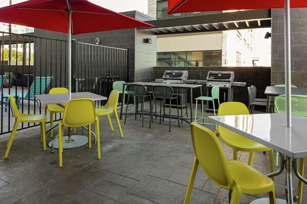 An outdoor patio area with yellow chairs and tables, a grill, and a red umbrella.