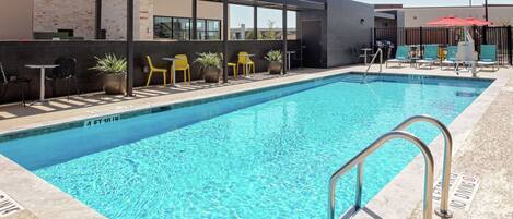 Una piscina rectangular con agua azul cristalina, rodeada de sillas amarillas y plantas en macetas.