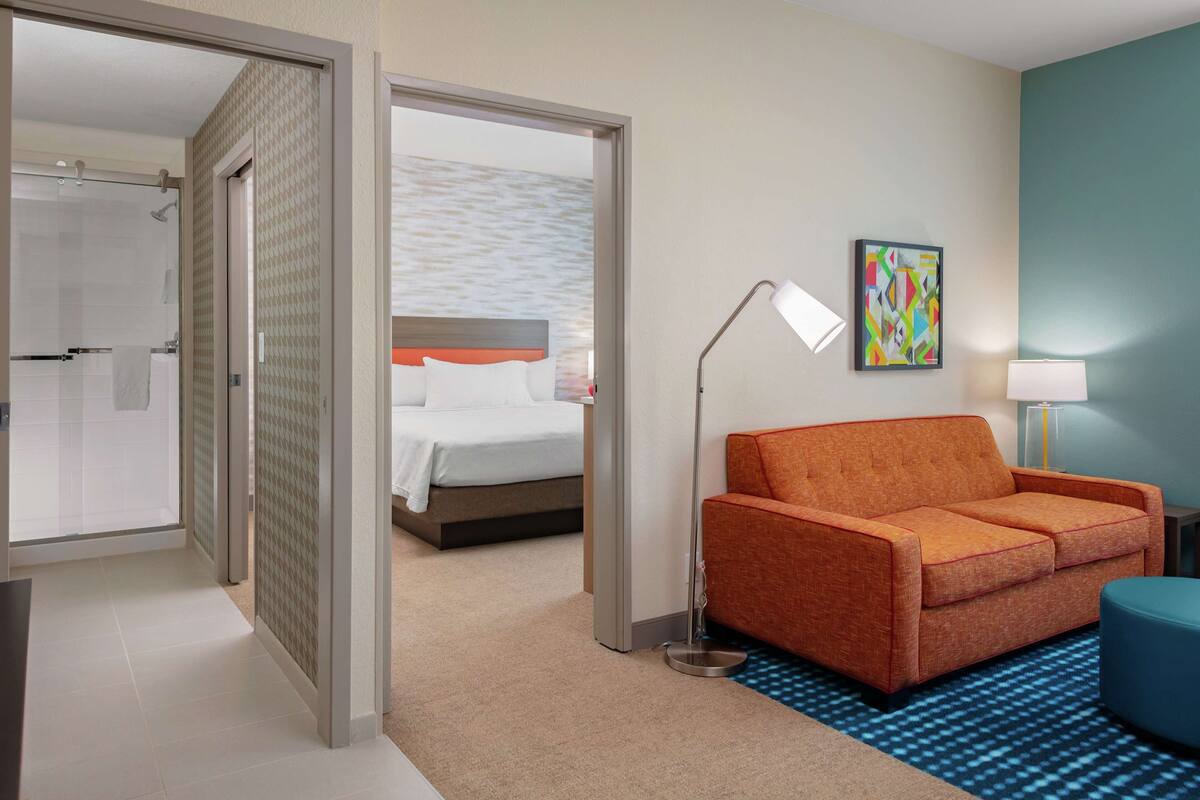 A hotel room with a bed, a sofa, a desk, a lamp, and a painting on the wall.